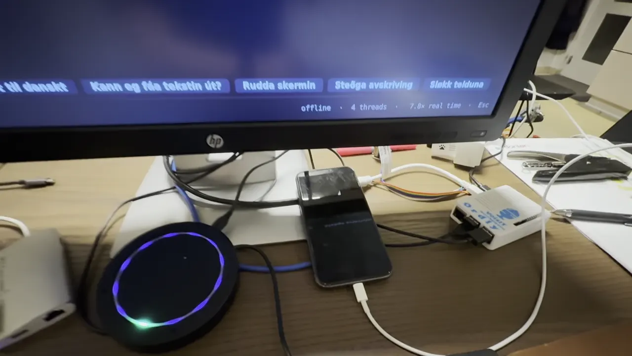 Mynd úr videoinum: ein rund mikrofon við bláum ljósi, ein lítil hvítur kassi og ein telefon á einum borði undir einum skermi.